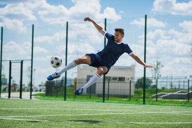 athletic soccer player kicking ball on soccer pitch