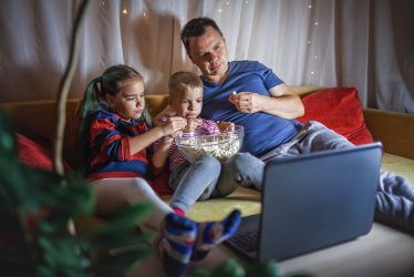 family movie night father with kids watching movie with popcorn by laptop indoor lifestyle